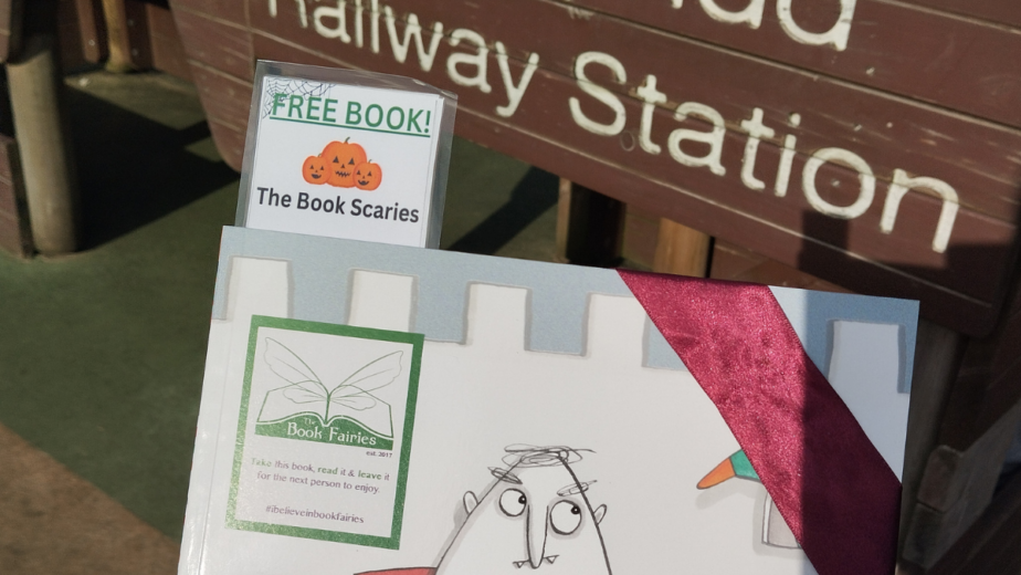 A book wrapped in ribbon being held infront of a sign that says 'Pontypridd Railway Station'