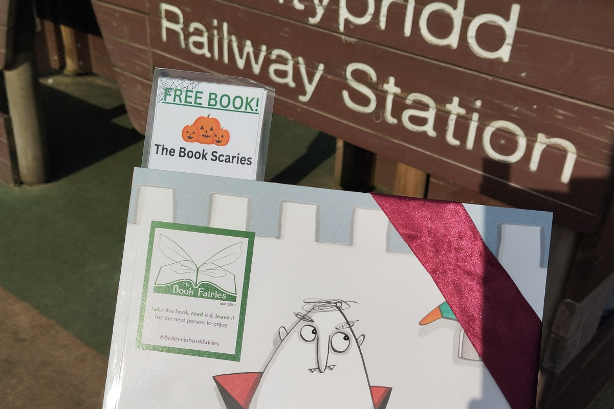 A book wrapped in ribbon being held infront of a sign that says 'Pontypridd Railway Station'
