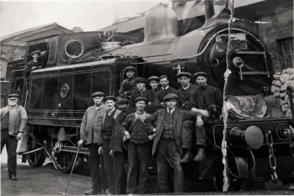 A black and white photo of railway workers standing infront of a big steam train