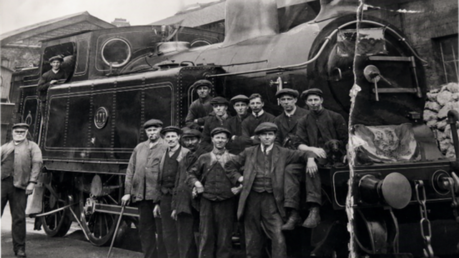 A black and white photo of railway workers standing infront of a big steam train