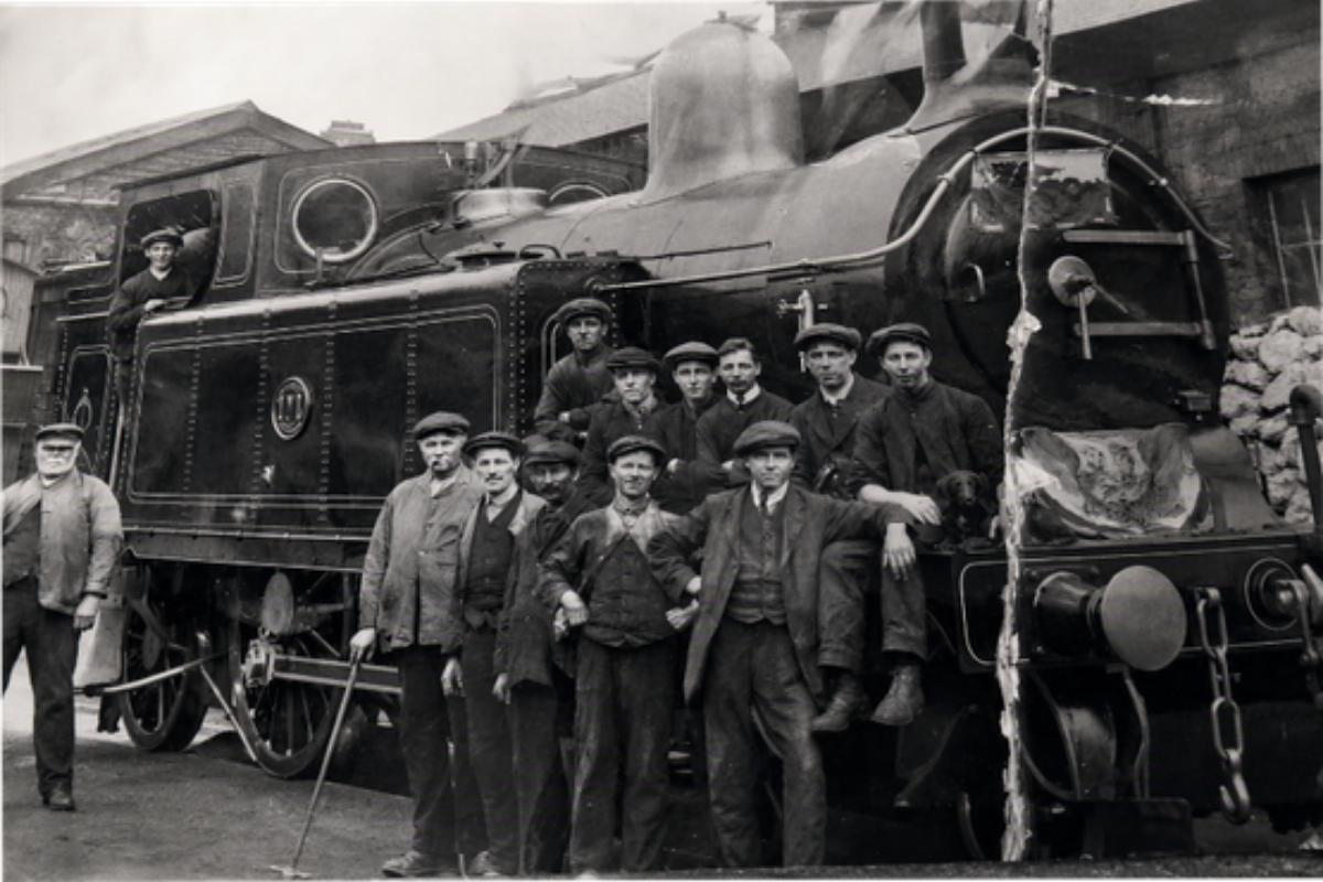 A black and white photo of railway workers standing infront of a big steam train