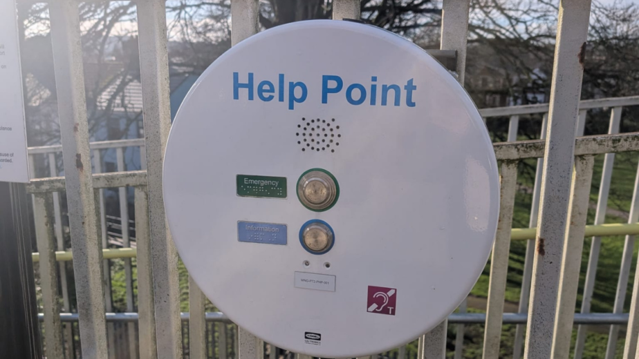 A white round machine on railings that says 'Help Point' and two buttons that say 'Emergency' and 'Information'