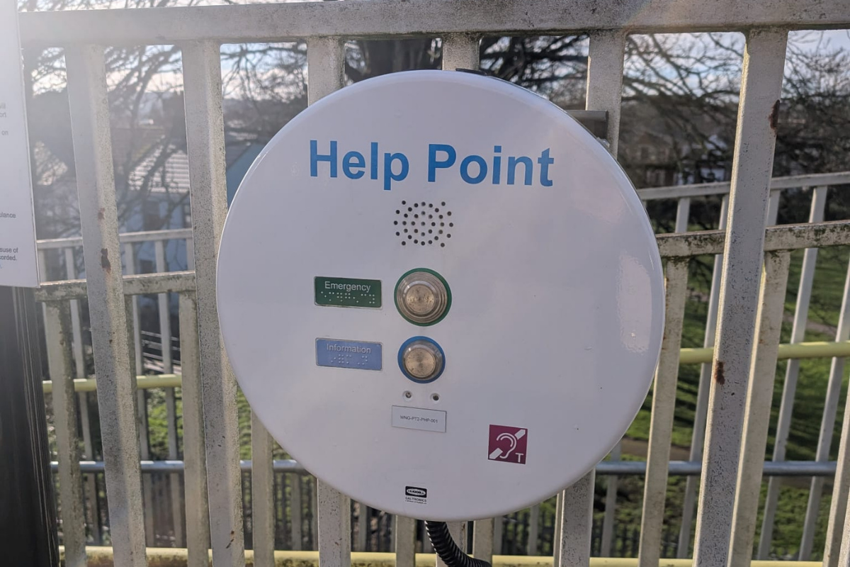 A white round machine on railings that says 'Help Point' and two buttons that say 'Emergency' and 'Information'